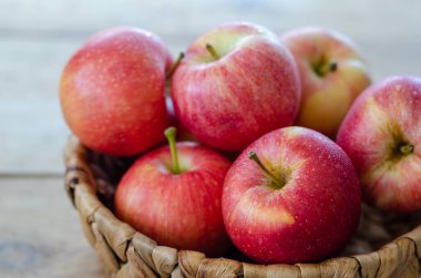 Kırmızı elmalar sepetin içinde, ahşap masanın üstünde.