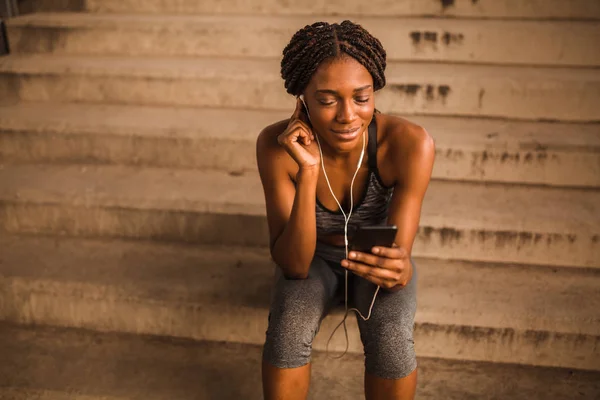 Young african american female runner resting on stairs and listening to her favorite music