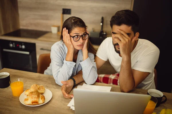 Young couple is having troubles with documentation which they analyzing while having breakfast in kitchen