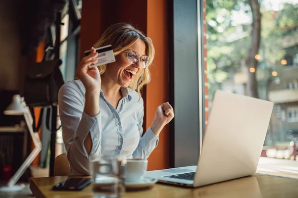 Gözlüklü güzel sarışın kadın kafeteryada oturan ve laptop ve kredi kartı ile alışveriş online