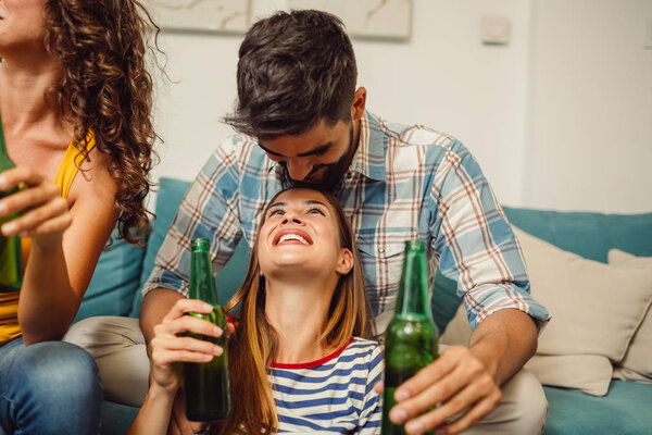 Close shot of young couple who is drinking beer together with their friends at home party