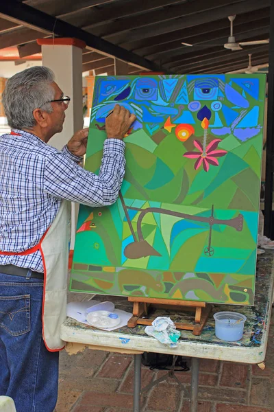 Soyut Ressam At Work.Older, modern giyimli, erkek sanatçı sanat stüdyosunun terasında soyut resim çiziyor. Çalışmalarında mavi, yeşil ve kahverengi şekiller kullanır. Puerto Vallarta eski kenti, Meksika.