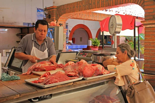 墨西哥瓦利亚塔港 一位衣着考究 年事已高的老人在他位于瓦利亚塔港老城区公共市场的摊位上 用肉刀为他的顾客女士准备肉 — 图库照片