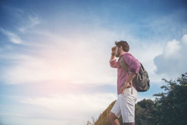 Yaz dağlarında, günbatımında uçurumun tepesinde duran ve doğanın tadını çıkaran genç adam.
