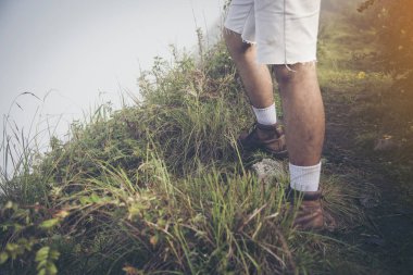 Yaz dağlarında, günbatımında uçurumun tepesinde duran ve doğanın tadını çıkaran genç adam.