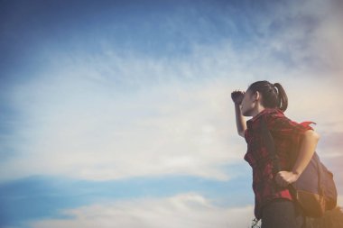 Sırt çantalı hippi genç kız sisli dağın zirvesinde günbatımının tadını çıkarıyor. Arka planda turist modeli var. Gezgin gün ışığına bakıyor