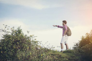 Yaz dağlarında, günbatımında uçurumun tepesinde duran ve doğanın tadını çıkaran genç adam.