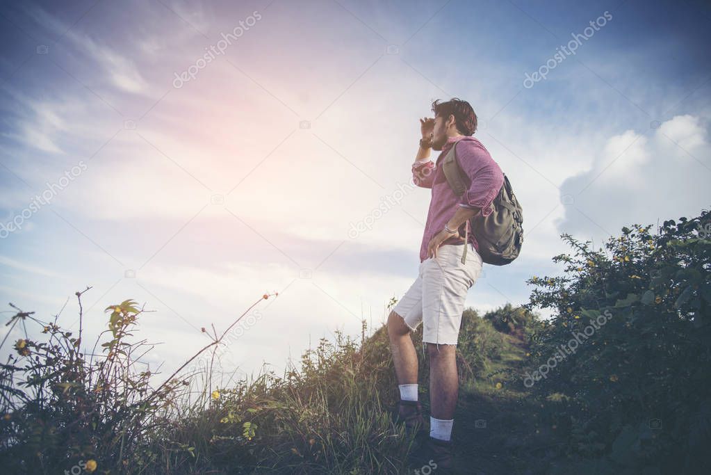 Young man standing on top of cliff in summer mountains at sunset