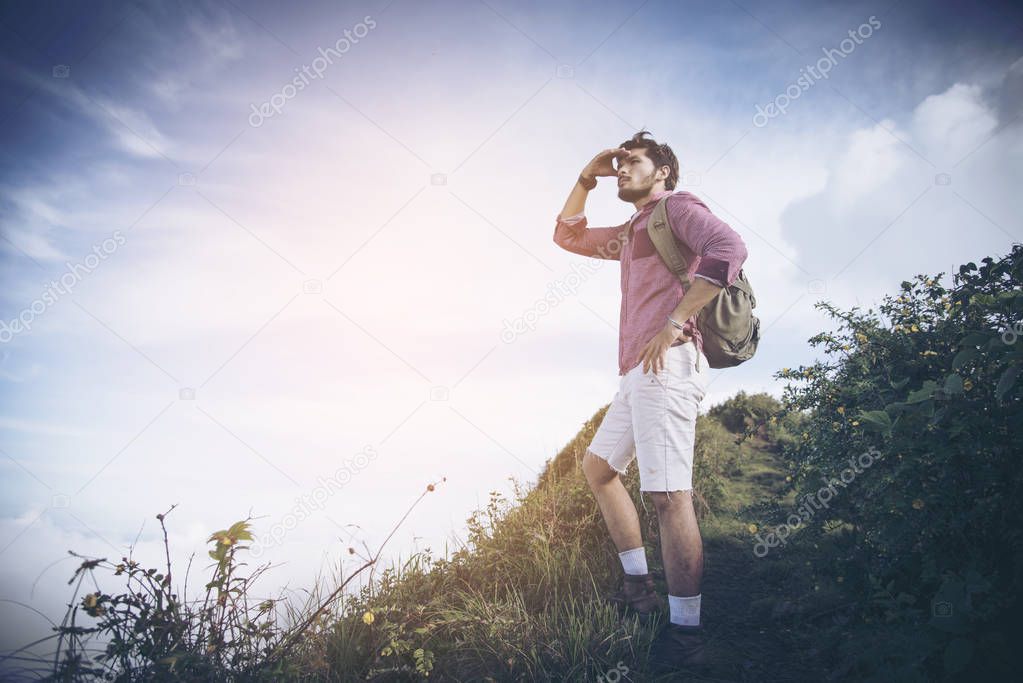 Young man standing on top of cliff in summer mountains at sunset