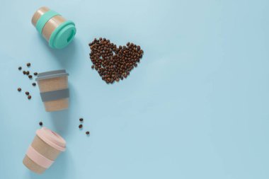 Mavi arka planda kahve çekirdeği kalpli tekrar kullanılabilir kahve fincanları. Sıfır atık kavramı. Yüksek kaliteli fotoğraf.