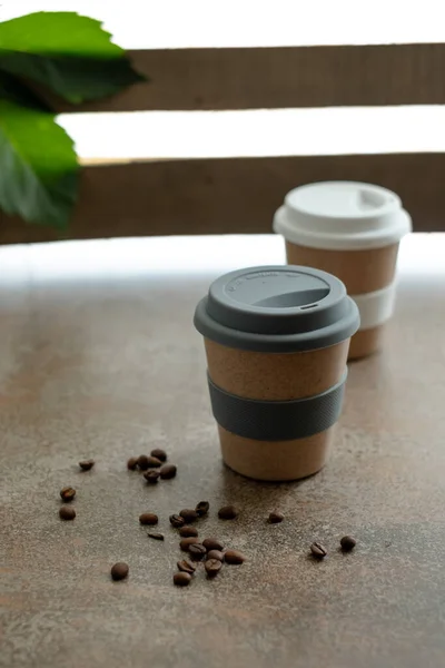 Reusable cups of coffee or tea with lids, coffee beans scattered on the table