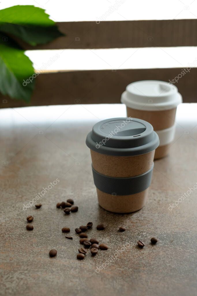 Reusable cups of coffee or tea with lids, coffee beans scattered on the table 