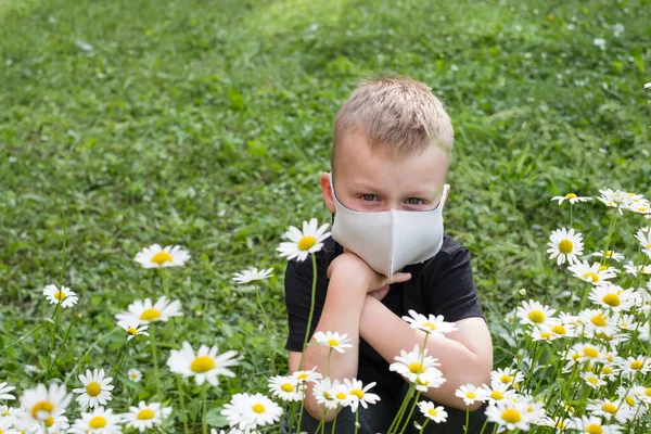 The boy is sitting near the chamomile in a mask, watery eyes. childrens allergy.children and flowers — Stock Photo, Image