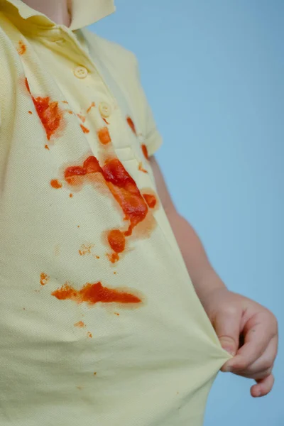 Het kind trekt een T-shirt met vlekken uit ketchup — Stockfoto