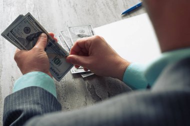 Bir adam masada 100 dolarlık banknotlar, boş bir kağıt ve masada bir dizüstü bilgisayar sayar. Yüksek kalite fotoğraf