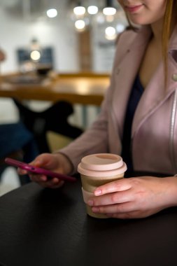 Genç beyaz kız kahve içiyor ve kafede akıllı telefon kullanıyor. Yüksek kalite fotoğraf