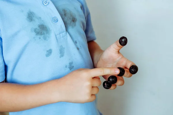 Black olives on each finger of a child\'s hand and is counting themOn the background of stains on a T-shirt. Isolated on a white background. High quality photo