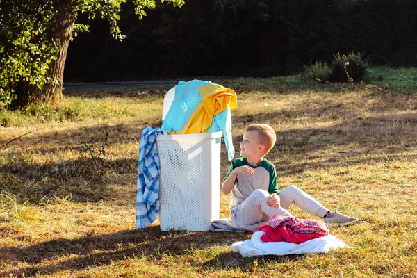 Das Kind Sitzt Neben Einem Korb Mit Schmutziger Kleidung Draußen — Stockfoto