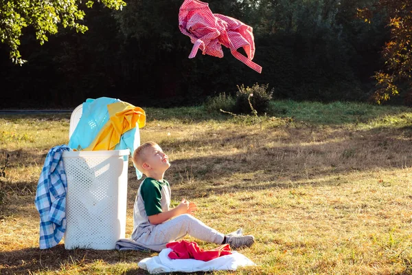 Das Kind Sitzt Neben Einem Korb Mit Schmutziger Kleidung Draußen — Stockfoto