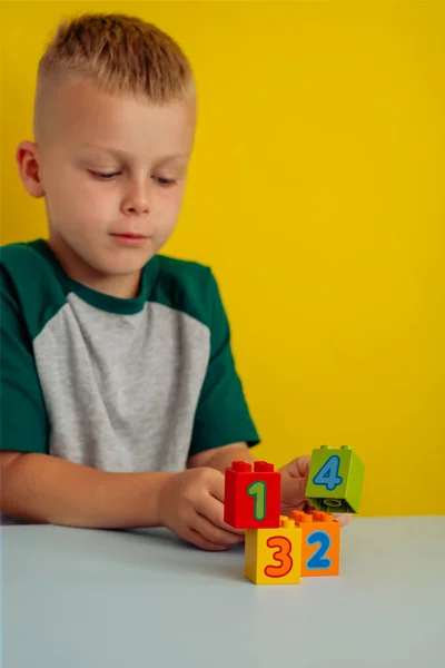 El niño jugando con cubos con números en la mesa.Sobre un fondo amarillo.Concepto de desarrollo infantil temprano —  Fotos de Stock