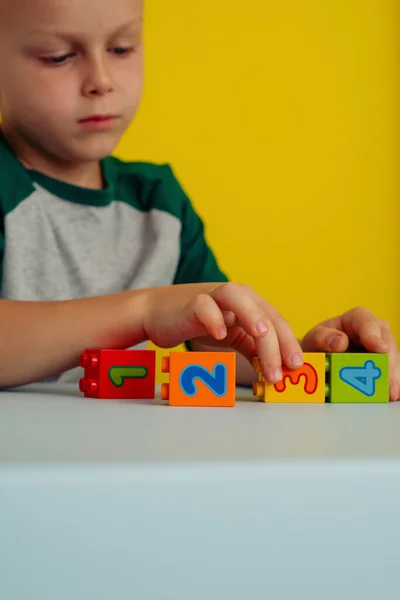 The child playing with cubes with numbers on the table.On a yellow background.Concept of early child development — Stock Photo, Image