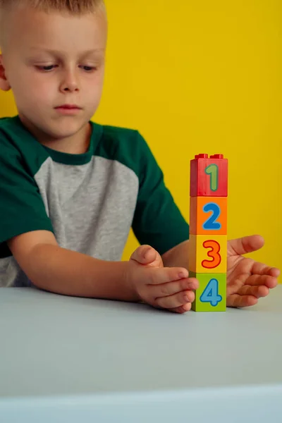 A criança brincando com cubos com números na mesa.Em um fundo amarelo.Conceito de desenvolvimento infantil precoce — Fotografia de Stock