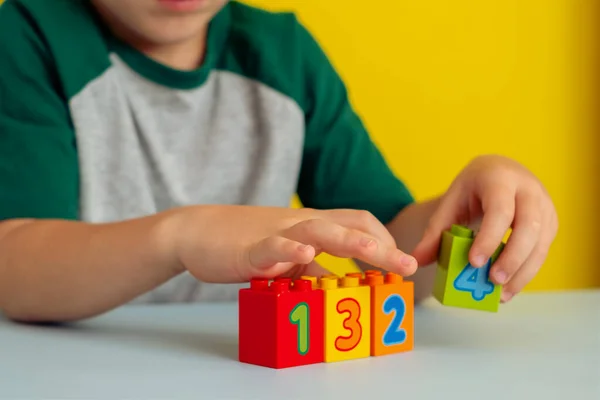 Primer plano de las manos de los niños jugando cubos de colores con números en la mesa.Sobre un fondo amarillo.Concepto de desarrollo infantil temprano. Foto de alta calidad — Foto de Stock