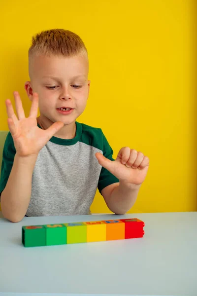 Menino contando com o dedo na mesa figuras coloridas blocks.On um fundo amarelo — Fotografia de Stock