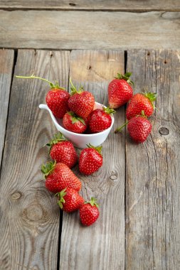 Eski ahşap desenli bir masanın üstünde sulu organik çilekler.