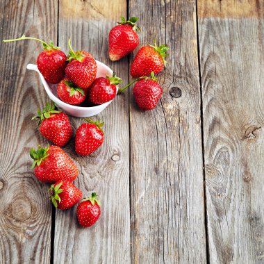 Eski ahşap desenli bir masanın üstünde sulu organik çilekler.