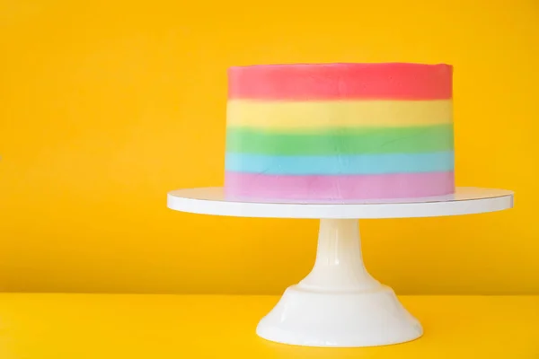 Cake blank with colorful rainbow cream on a yellow background decorated with colorful sprinkles, poured with chocolate. Simple minimalism.