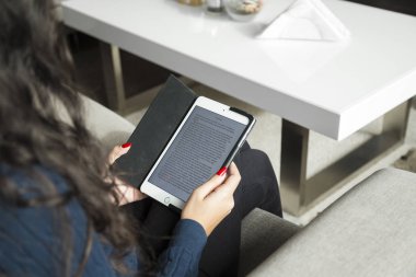Oturma odasında bir kanepede oturan ve onun ipad ile ilgili bir kitap okuma genç bir kadın.