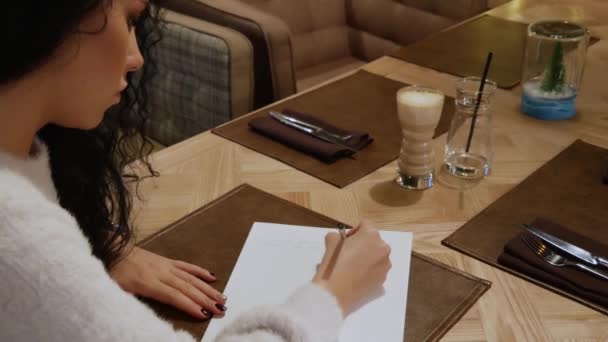 Jolie fille brune aux cheveux bouclés écrit un poème dans un restaurant — Video