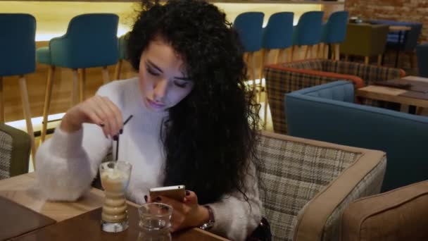 Señora con el pelo rizado en un restaurante está trabajando en el teléfono y beber café — Vídeo de stock