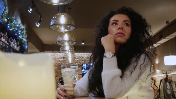 Красивая кудрявая девушка ждет в ресторане и смотрит на часы — стоковое видео