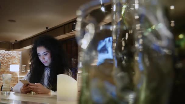 Belle fille aux cheveux bouclés dans un restaurant travaille sur le téléphone — Video