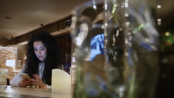 Belle fille avec les cheveux bouclés dans un restaurant travaille sur le téléphone et sourire — Video