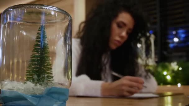 Árbol de año nuevo en vidrio con hermosa chica escribiendo una carta en el fondo — Vídeos de Stock