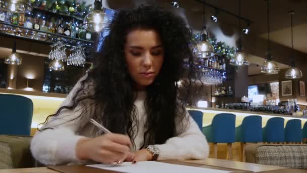 Attraktives Mädchen mit lockigem Haar malt ein Herz in einem Restaurant — Stockvideo
