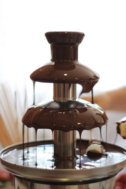 Fruit on a stick under the dripping chocolate in a chocolate fountain clipart