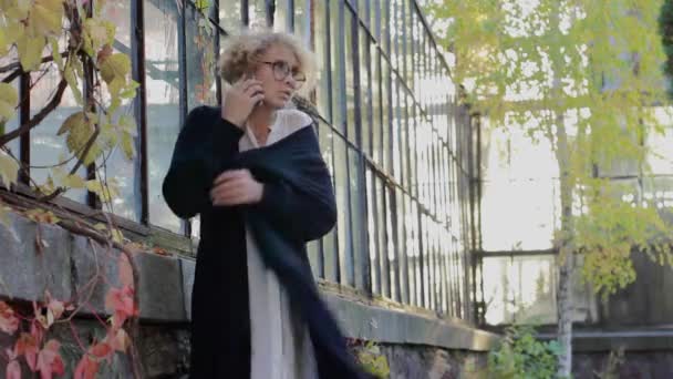 De blonde met een bril op de telefoon spreekt en bevriest — Stockvideo