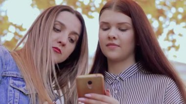 İki güzel gülümseyen kız telefon sonbahar parkta bakıyorsun