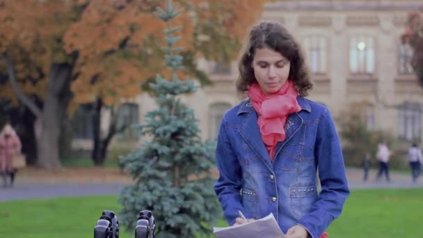 Vrouw schrijver neemt notities op papier in het park — Stockvideo