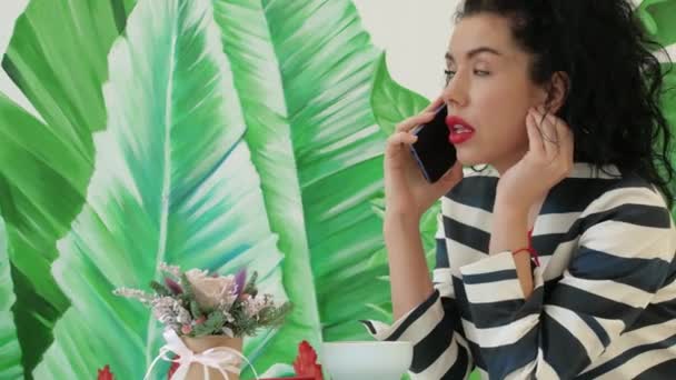Joven, hermosa mujer en un traje a rayas hablando por teléfono en el fondo de hojas verdes — Vídeos de Stock