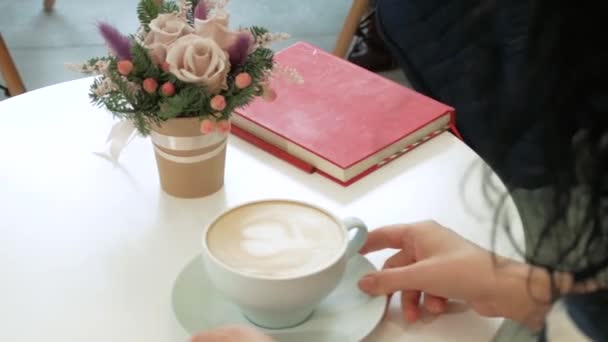 Mujer sostiene una taza de capuchino con un corazón en la crema — Vídeo de stock