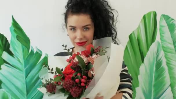 Beautiful curly woman with a gorgeous bouquet on the background of painted green leaves — Stock Video