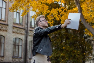 Rahat giysiler içinde Mutlu akıllı öğrenci kağıtları tutar ve uzağa bakar