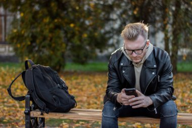 Rahat kıyafetler, bankta oturan bir telefon ile gülümseyen adam rüya