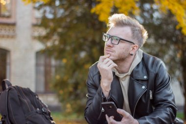 Bir telefon ile rahat giysiler içinde bir rüya akıllı adam bir bankta oturuyor