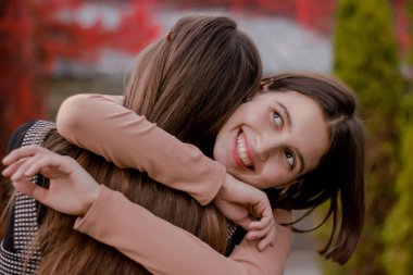 Kız kız arkadaşına sıkıca sarılır. Mutlu güzel öğrenci sonbahar parkta bir arkadaşı karşılamak için mutlu